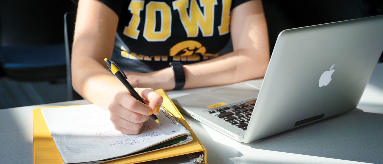 Iowa student writes notes while studying in front of laptop