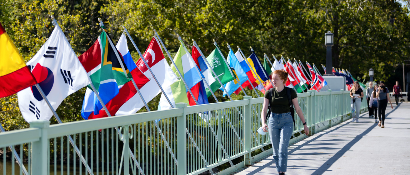 Woman walks in on Iowa Memorial Bridge in front of various countries' flags