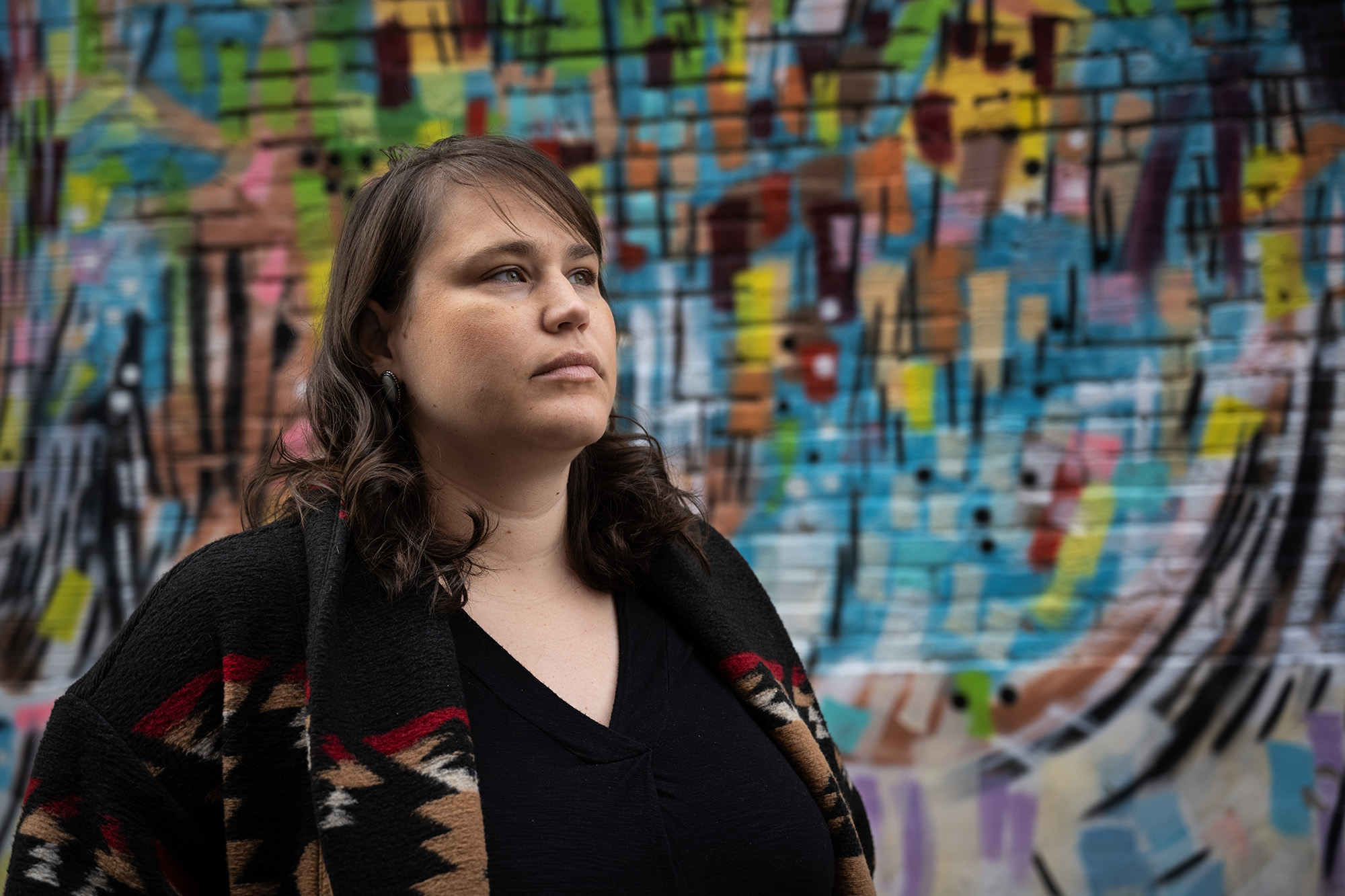 University of Iowa graduate Carrie Schuettpelz looks beyond the frame standing in front of a colorful mural