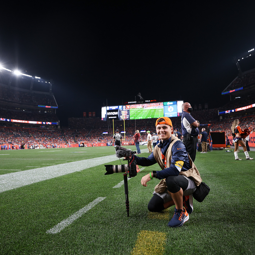 Intern for the Denver Broncos and Hawkeye, Cole Cooper neils with a camera on an NFL football field