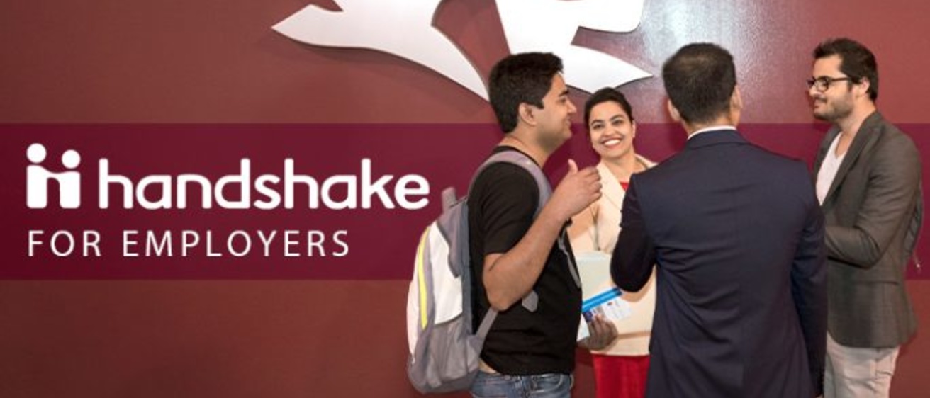 people talking in front of a wall with the Handshake logo