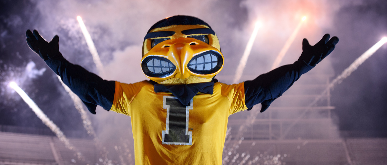 herky raises his arms with fireworks behind him