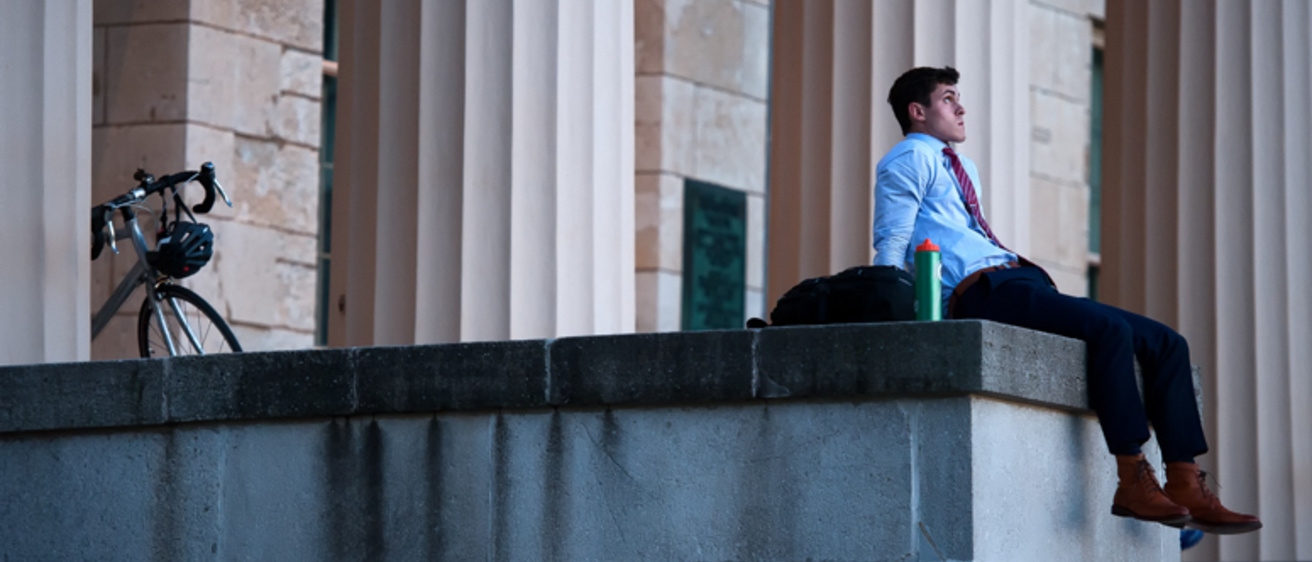 student in suit and tie sits on old capitol steps