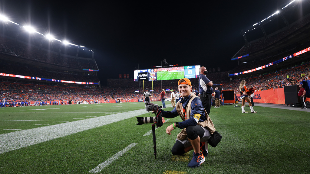 Intern for the Denver Broncos and Hawkeye, Cole Cooper neils with a camera on an NFL football field
