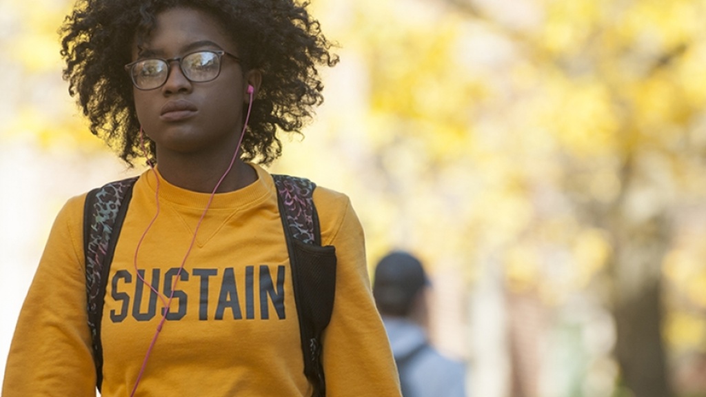 Student walks on campus with shirt that says the words "Sustain"