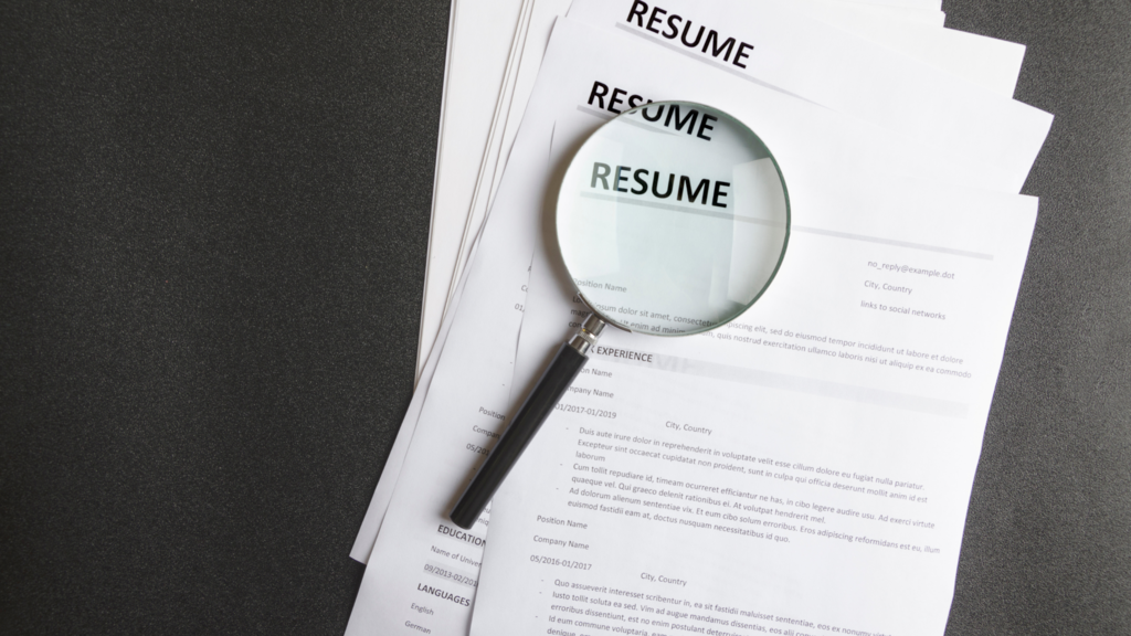 magnifying glass sits on stack of resumes